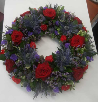 Quintessentially Scottish - This beautiful wreath has a truly scottish feel. It includes our national flower, the thistle, teamed with luxurious red roses, purple limonium-which mirrors the highland heather, lush green foliage and adorned with tartan ribbon throughout.

